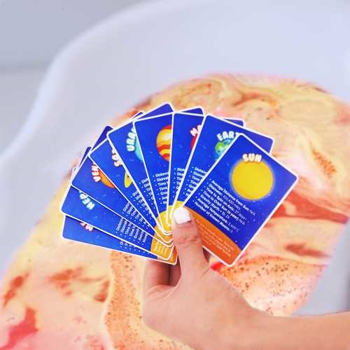 Mão a segurar os cartões de factos planetários incluídos no ZIMPLIKIDS Pack Bombas de banho.