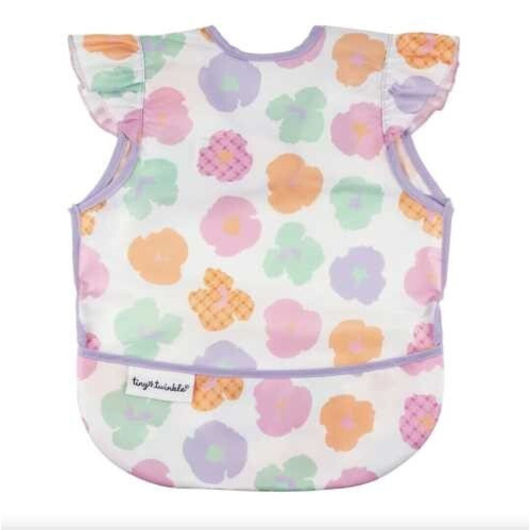 Babete impermeável da Tiny Twinkle com padrão de flores em tons pastéis (rosa, lilás, verde, laranja) e folhos nos ombros, com bolso apanha-migalhas.