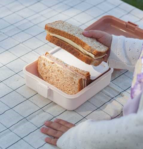 Mão de uma criança a colocar uma sandes na lancheira Monbento Snacky, demonstrando a sua capacidade para lanches.