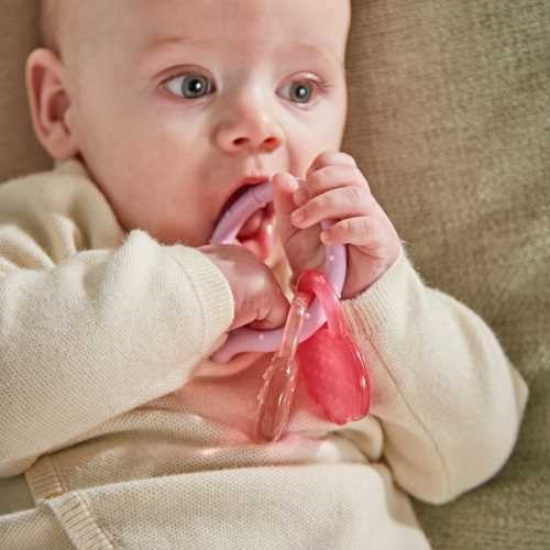 Bebé a segurar e a morder o mordedor Matchstick Monkey de silicone, com as cores rosa e bege visíveis.