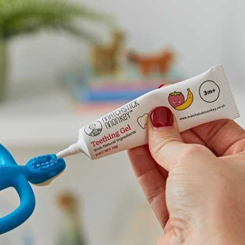 Uma mão a aplicar o gel de dentição Matchstick Monkey diretamente na parte superior do mordedor azul em forma de macaco.