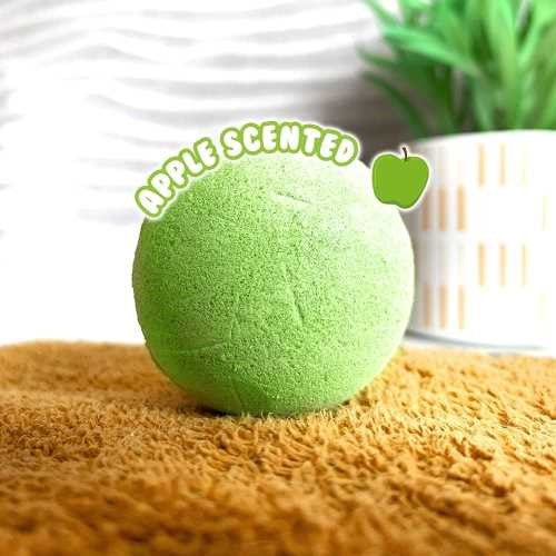 Uma bomba de banho ZIMPLIKIDS verde com a indicação "Apple Scented" (aroma a maçã) em destaque, pousada numa toalha castanha.