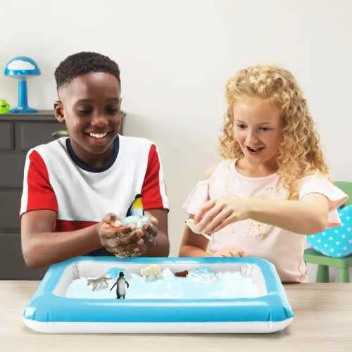 Duas crianças sorridentes a brincar com a neve artificial e as figuras de animais do kit ZIMPLIKIDS Pack Snow Adventures na bandeja.