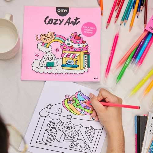 Livro OMY Cosy Art Kawaii em uso, com lápis de cor e uma ilustração a ser colorida.