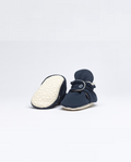 Pantufas pretas com solas expostas, destacando o seu design antiderrapante e adaptável para bebés que começam a caminhar.
