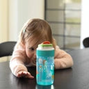 Criança pequena com cabelo loiro a olhar para a Garrafa Kambukka LAGOON Disco Zoo 400ml em cima de uma mesa escura, mostrando o seu tamanho para uso infantil.