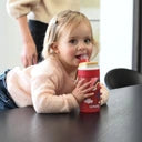 Uma menina pequena a beber de uma garrafa Kambukka LAGOON Love Birds 400ml, enquanto está deitada numa mesa.