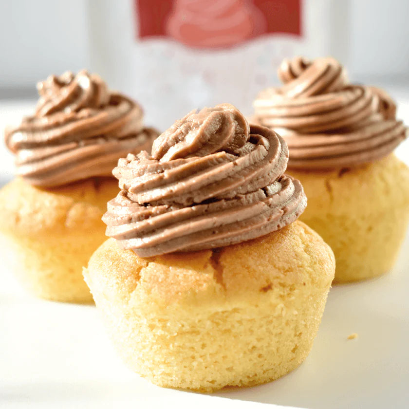 Três cupcakes com cobertura generosa de buttercream de chocolate Fidu, montados sobre bases de bolo claro.