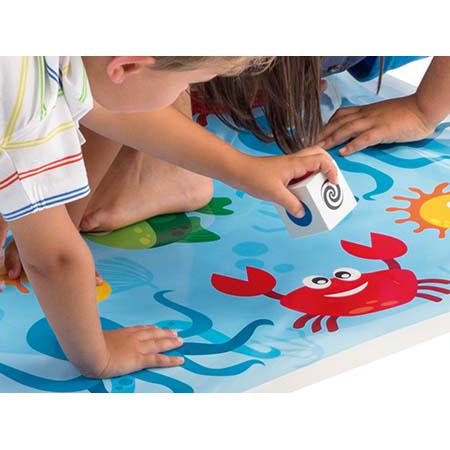 Criança a rolar o dado grande com símbolos no tabuleiro azul do jogo Cayro Crisscross, com desenhos de vida marinha.