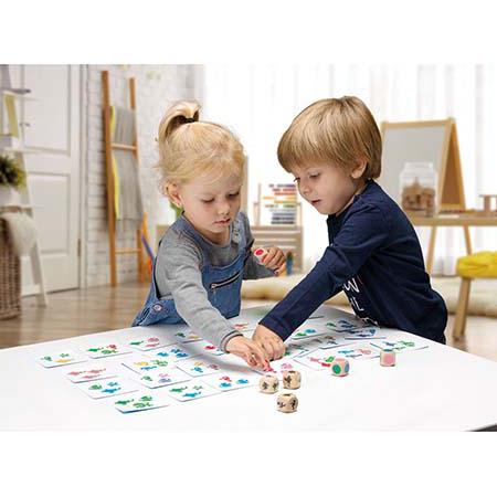 Duas crianças sentadas a uma mesa a jogar entusiasticamente o jogo Chaf Chof, apontando para as cartas no centro.