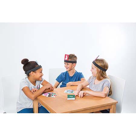 Três crianças a jogar o jogo Cayro "O que vês?" à volta de uma mesa, com tiaras na cabeça.