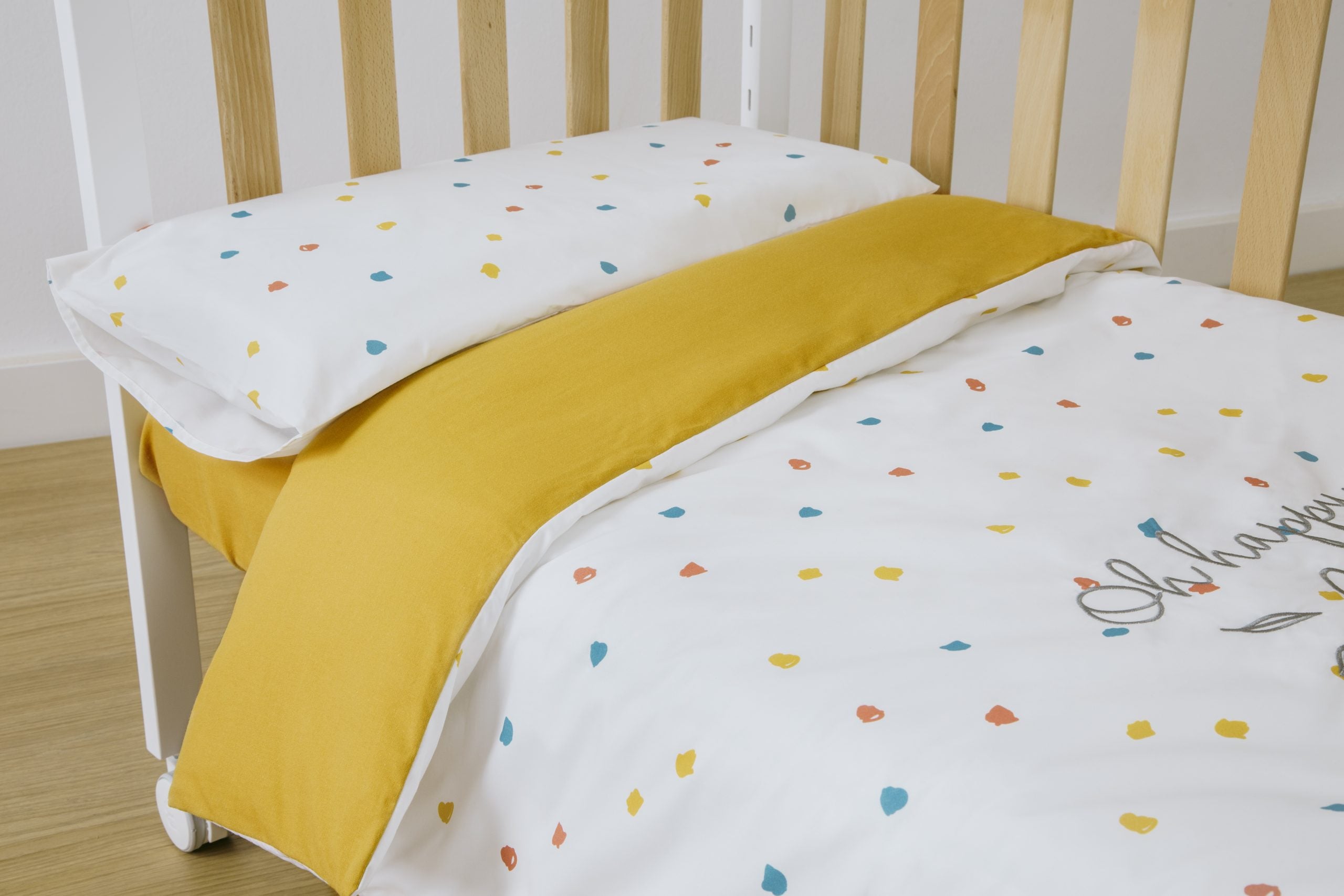 Conjunto de protetor e edredom Micuna Happy 120x60 para berço, com lado reversível amarelo e padrão de confetis coloridos.