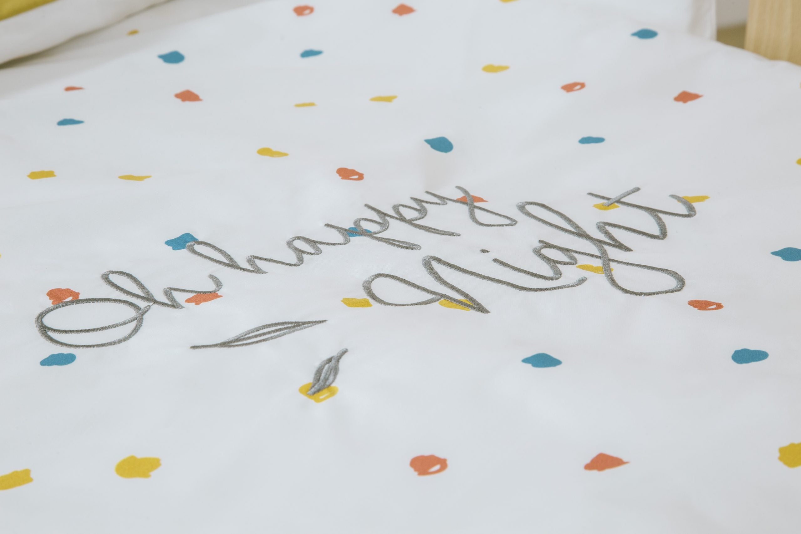 Detalhe do edredom Micuna Happy 120x60 com a inscrição bordada "Oh happy night" e padrão de confetis coloridos.