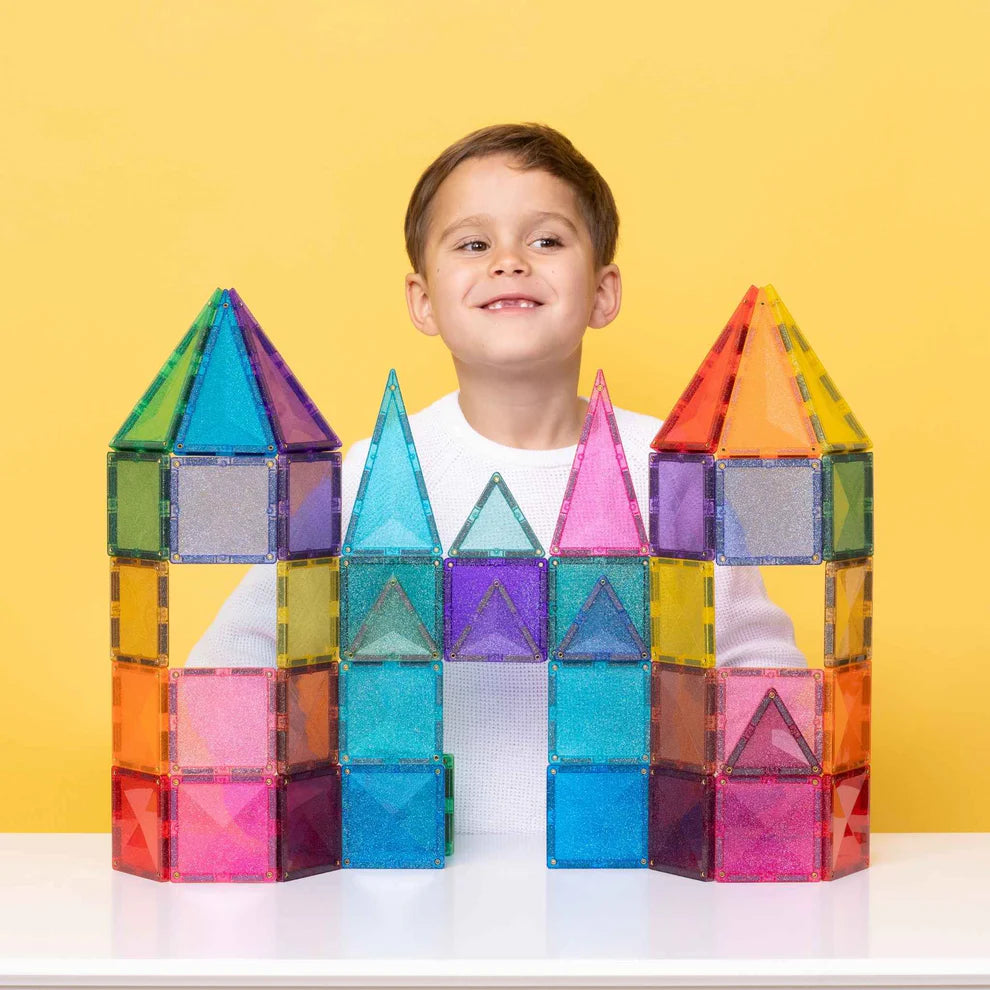 Menino feliz a brincar com um castelo colorido de blocos magnéticos Connetix Glitter Castle Pack, com torres pontiagudas.