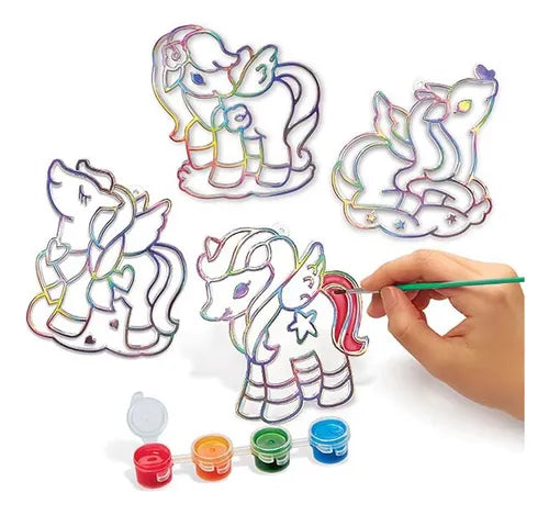 Quatro moldes de vitral de unicórnio, um dos quais está a ser pintado com tinta verde, acompanhado por pequenos recipientes de tinta colorida.