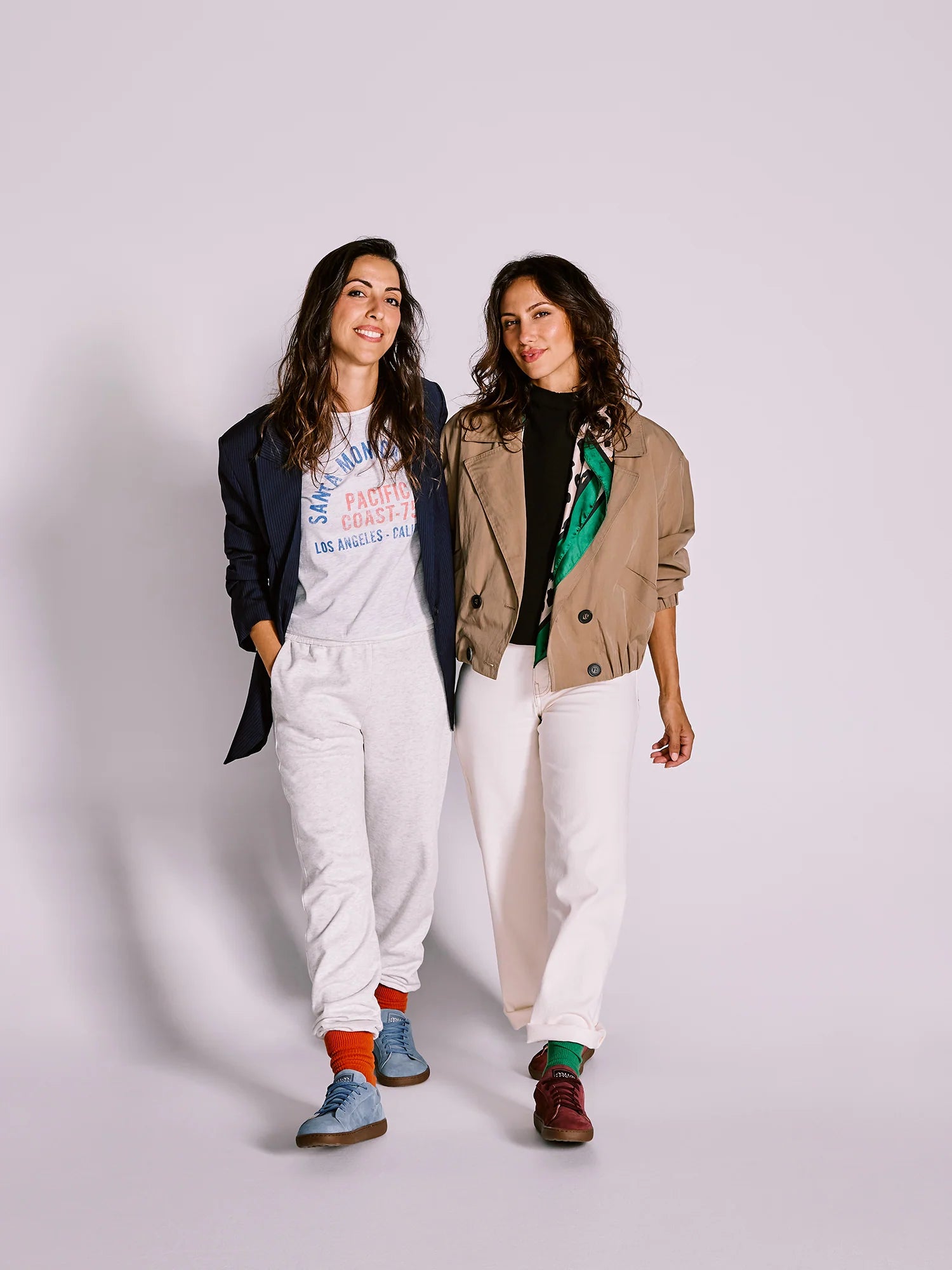 Duas mulheres sorridentes a caminhar, uma a usar sapatilhas MUM Barefoot Diana Wine bordô e outra sapatilhas azuis.