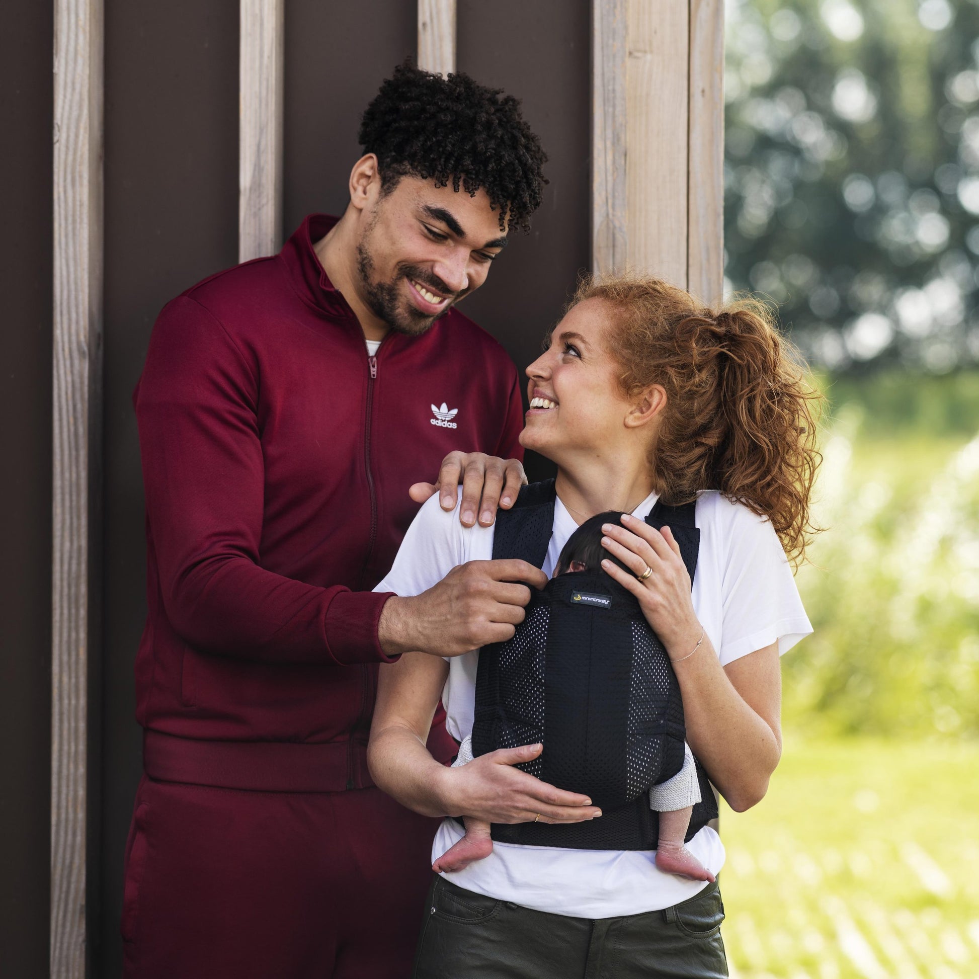 Casal a utilizar a Mochila Porta-bebés Minimonkey, sorrindo um para o outro, em ambiente rural.