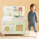 Menino sorridente ao lado da Classic World Natural Kitchen, exibindo a cozinha completa com fogão, forno, lava-loiça e máquina de lavar roupa.