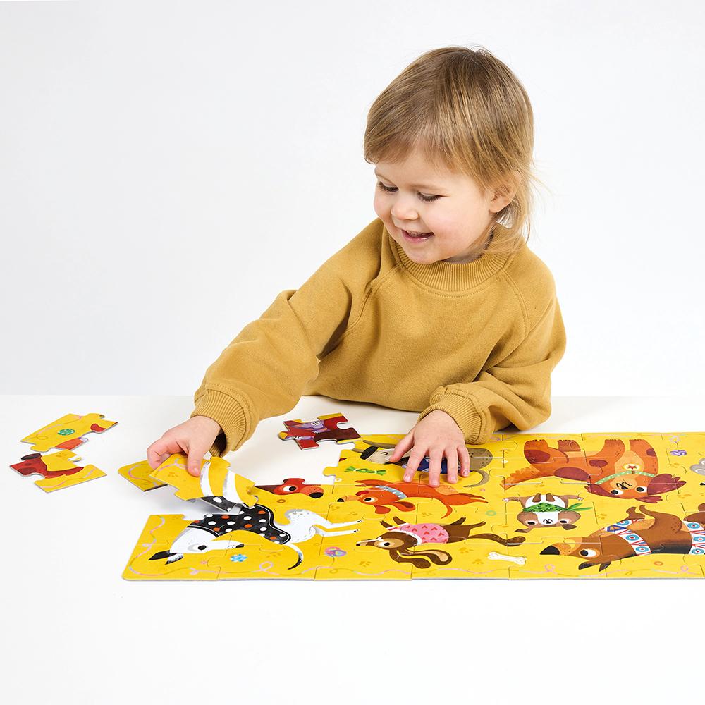 Criança sorridente com camisola amarela a montar o puzzle Banana Panda I Love Dogs, com peças coloridas de cães.