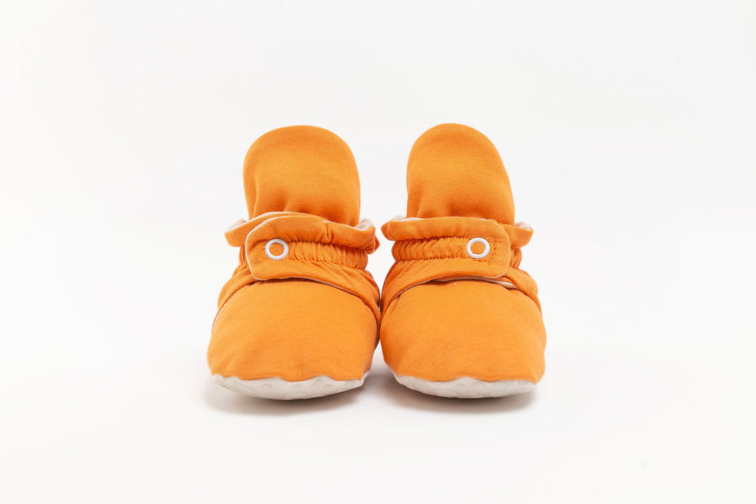 Pantufas botinhas cor de laranja para bebé, com molas de pressão e sola branca, sobre fundo branco.
