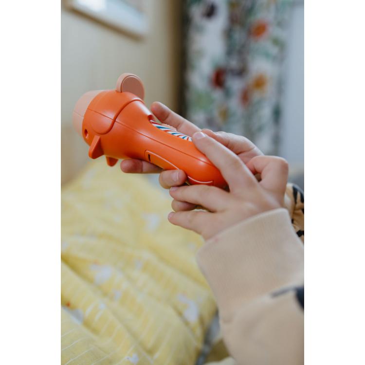 Mãos de uma criança a segurar e operar a lanterna projetor KidyWolf KIDYSLIDE laranja, focando na interatividade.
