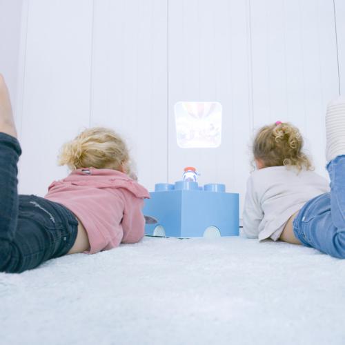 Duas crianças deitadas no chão, a observar uma imagem de foguetão projetada na parede pela lanterna KidyWolf.