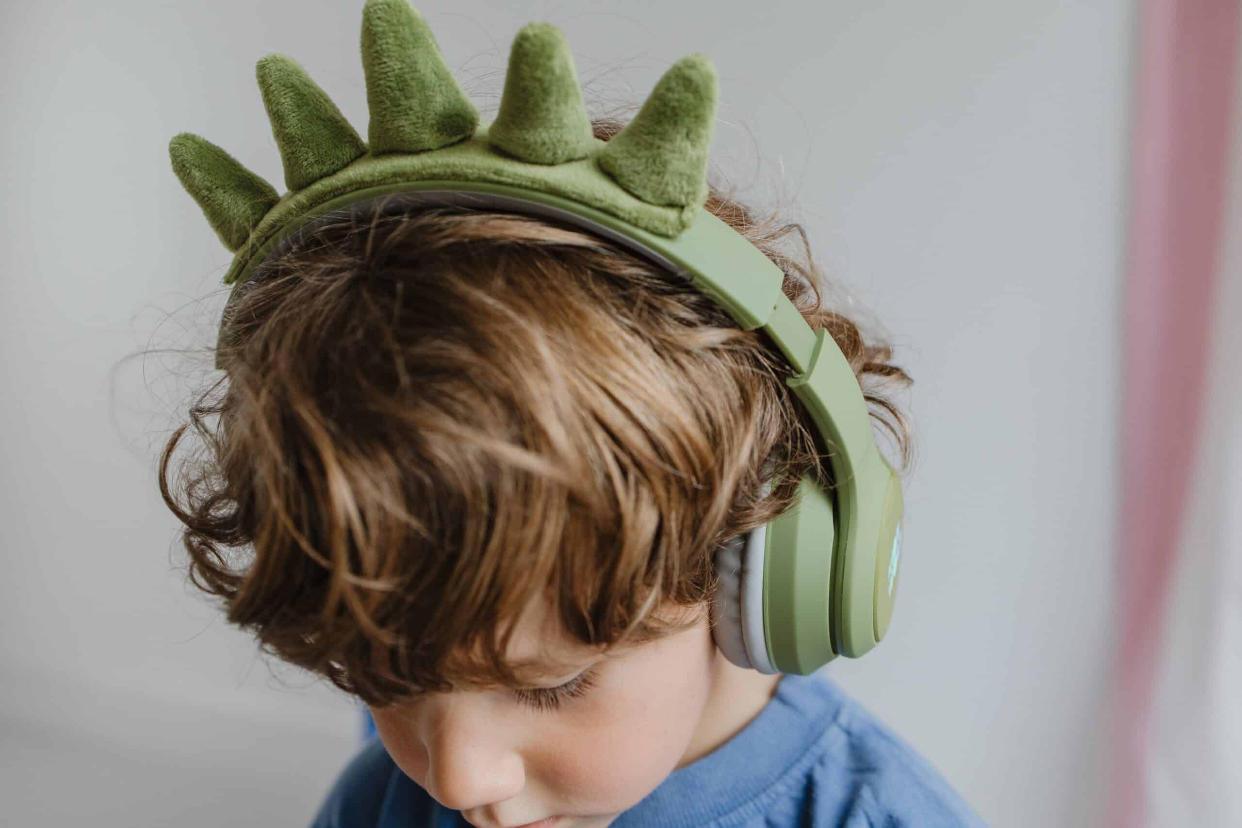 Criança a usar os headphones KidyWolf KIDYEARS verdes com orelhas de dinossauro, focando no conforto e design divertido para os mais pequenos.