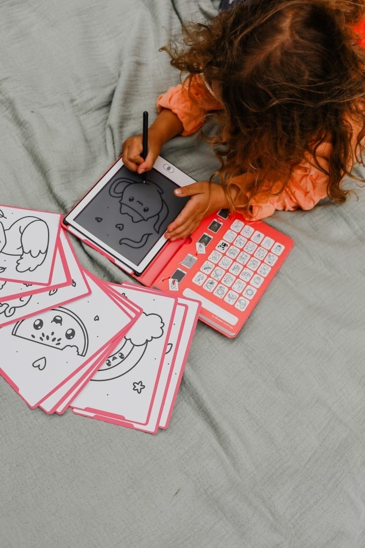 Criança a utilizar o tablet de desenho KidyWolf Kawai com a caneta stylus para traçar uma ilustração de um monstrinho fofo.