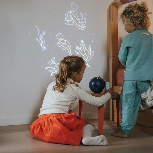 Duas crianças a observar as projeções de constelações no teto, utilizando o controlo remoto do projetor KidyStar.