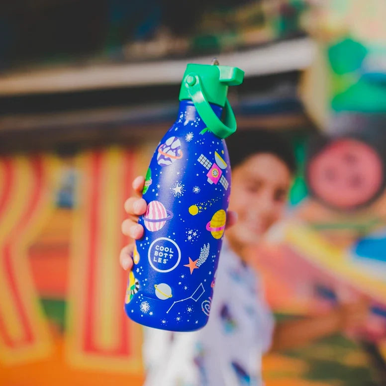 Pessoa segura a Garrafa Térmica Cool Bottles Stellar Journey 500ml com design de planetas e estrelas, em ambiente colorido.