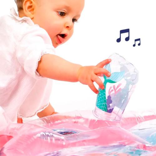 Um bebé a interagir com o Ludi Tapete de água Insuflável Sereia, tocando num copo transparente com design de cauda de sereia.