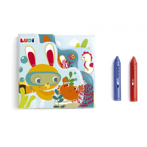 Ludi Livro de pintar no banho fechado, mostrando a capa com um coelho mergulhador e um caranguejo, ao lado dos dois lápis de cor vermelhos e azuis.