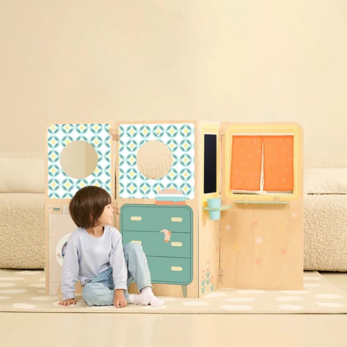 Criança sentada em frente à Classic World Mini Casa, com detalhes da lavandaria e outros espaços de brincadeira.