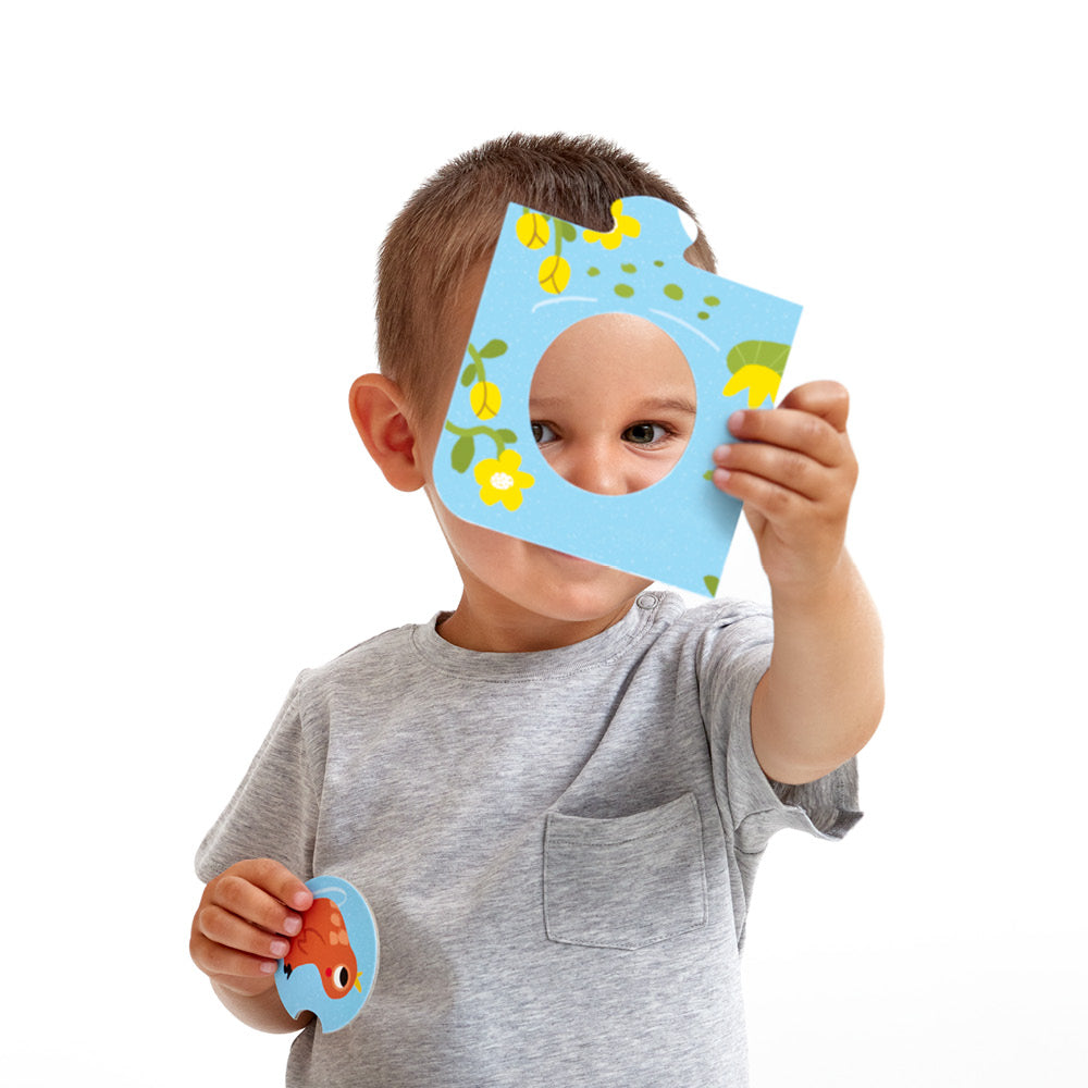 Criança a segurar uma peça de puzzle circular do Banana Panda Animais da Quinta à frente do rosto, com um olho visível através do buraco.