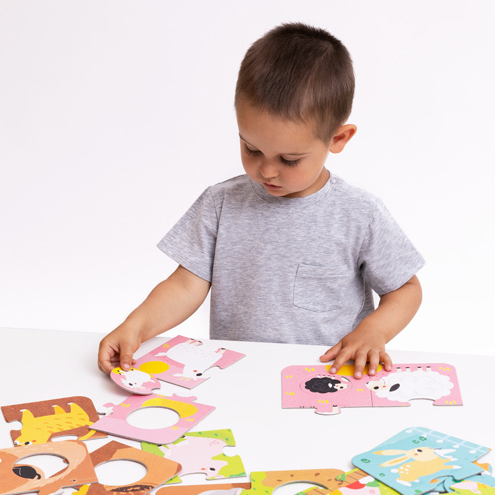 Criança a montar um dos puzzles de ovelhas do Banana Panda Puzzle de Correspondência Animais da Quinta, com outros puzzles espalhados na mesa.