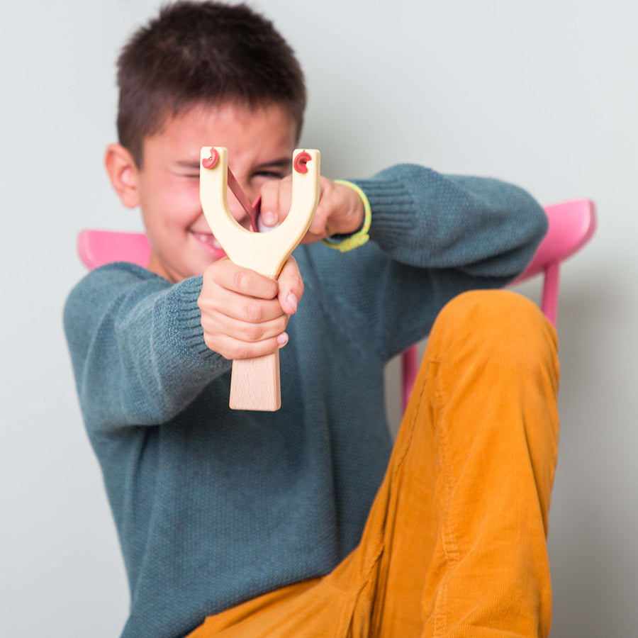 Menino a brincar com uma fisga de madeira da marca Me&Mine. Brinquedos tradicionais e de pontaria para crianças a partir dos 6 anos.