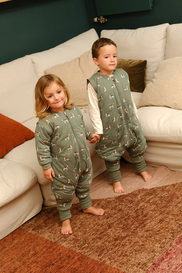 Duas crianças a usar sacos de dormir MolisandCo TOG 2.5 com pés e mangas, em casa, uma com padrão de cães e outra de girafas.