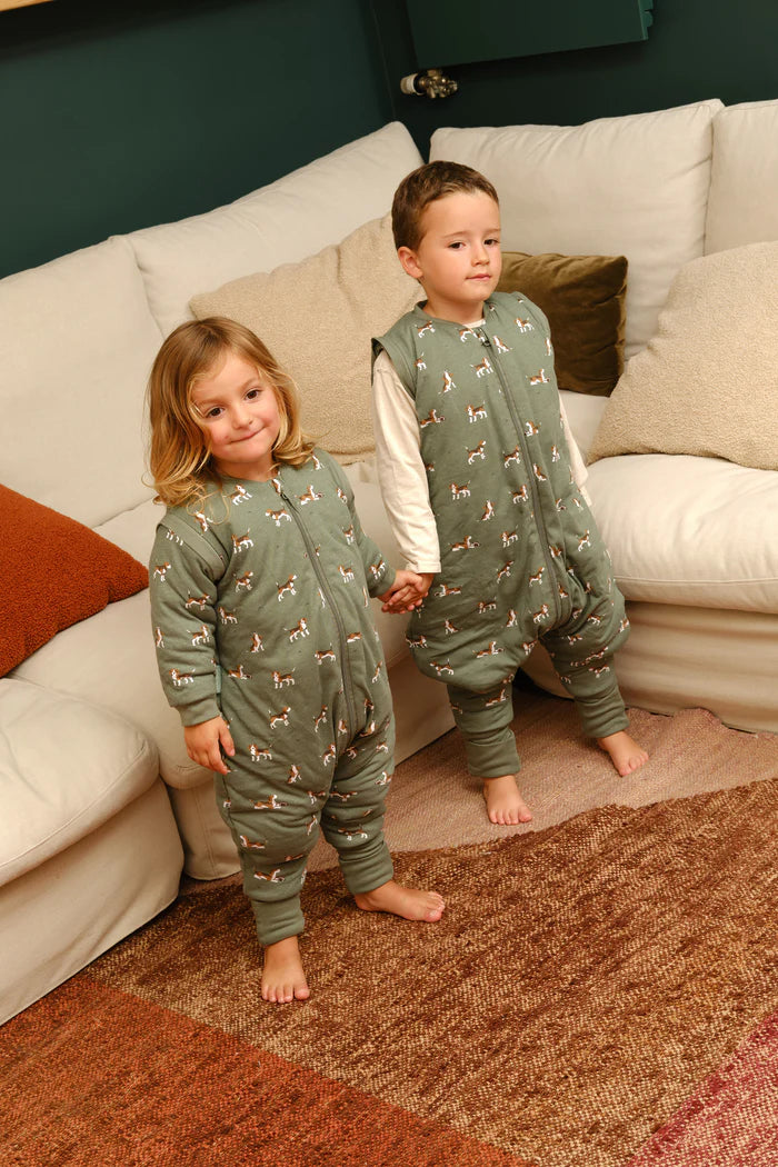 Duas crianças a usar sacos de dormir MolisandCo TOG 2.5 com pés e mangas, em casa, uma com padrão de cães e outra de girafas.