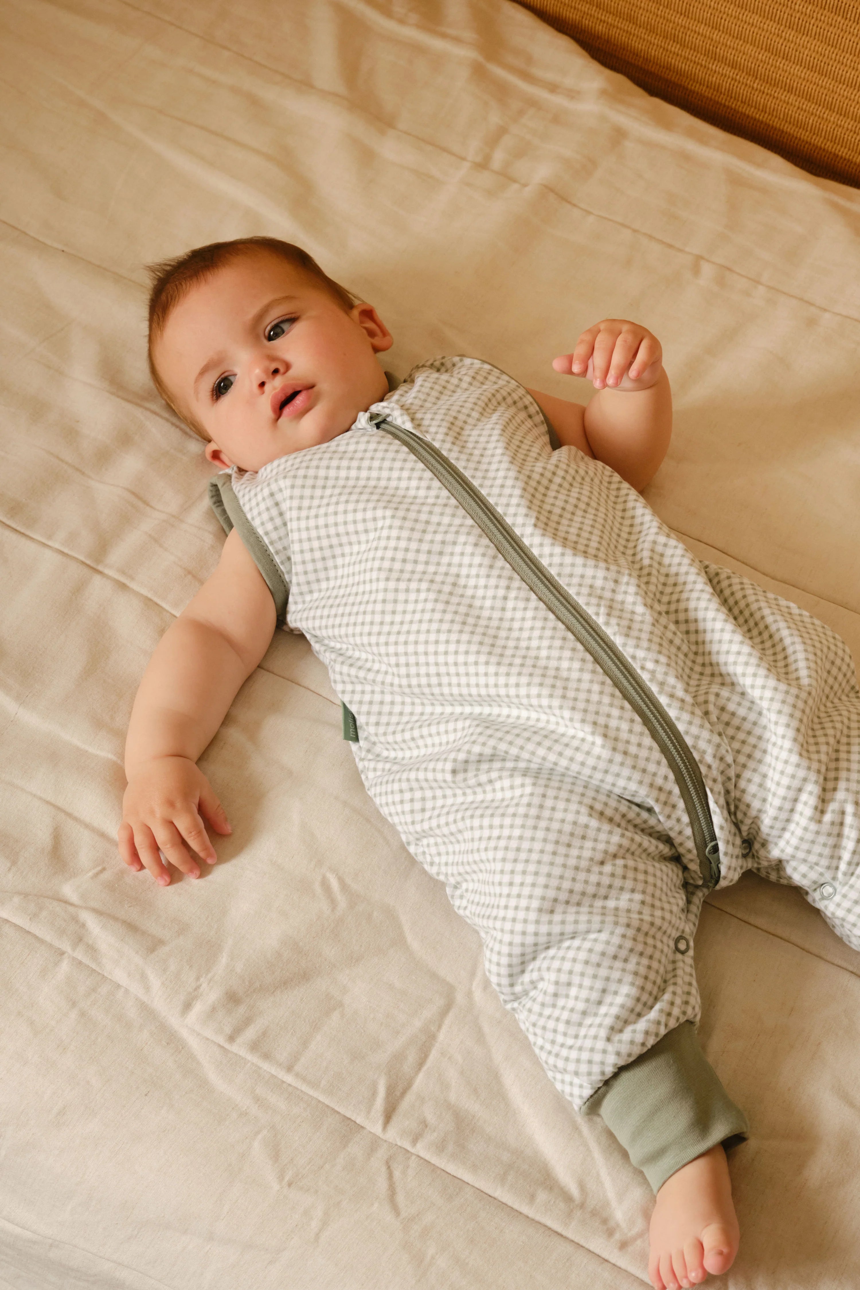 Bebé deitado de costas, vestindo o saco de dormir MolisandCo TOG 1.0 com pés VICHY GREEN, destacando o padrão e o fecho.
