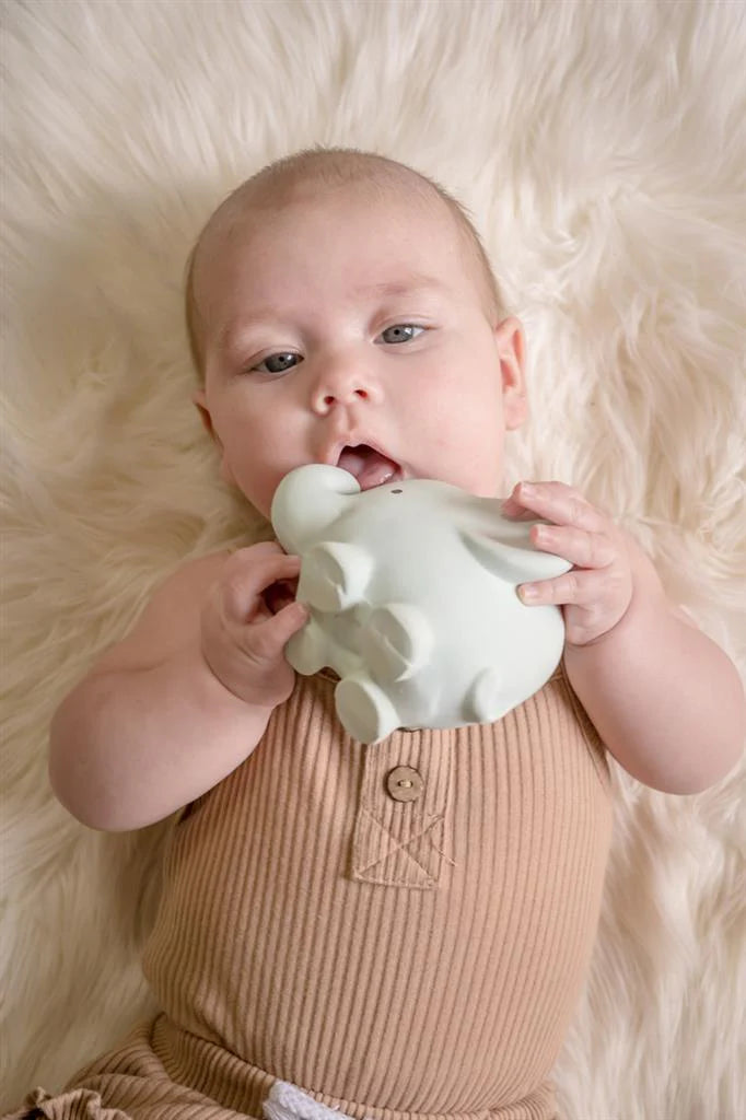 Bebé a segurar e a morder o mordedor em forma de elefante azul-claro da Tikiri, deitado sobre uma manta felpuda.