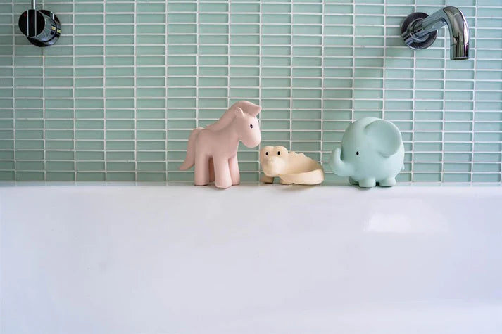 Os três mordedores da Tikiri alinhados na borda de uma banheira branca, com azulejos verde-água no fundo.