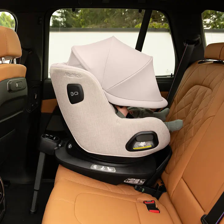 Cadeira auto Nuna Pruu Aire instalada no banco traseiro de um carro com estofos em pele castanha, vista de lado, com o bebé reclinado sob a capota.