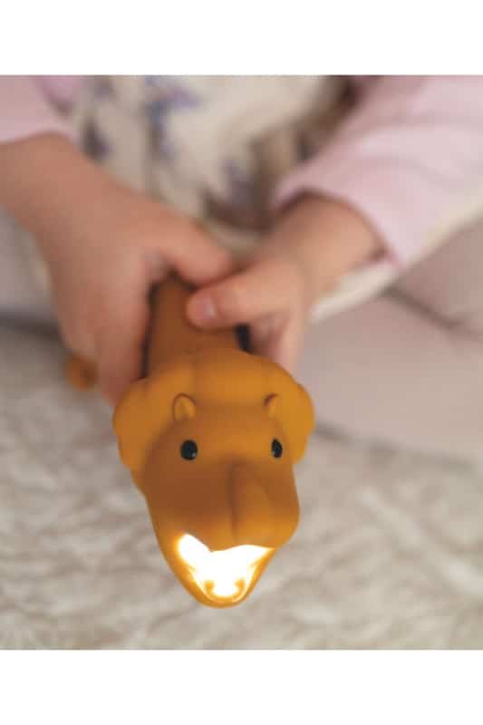 Mãos de criança segurando a lanterna Rabbit e Friends Leo, com a luz acesa na boca, criando um ambiente acolhedor.