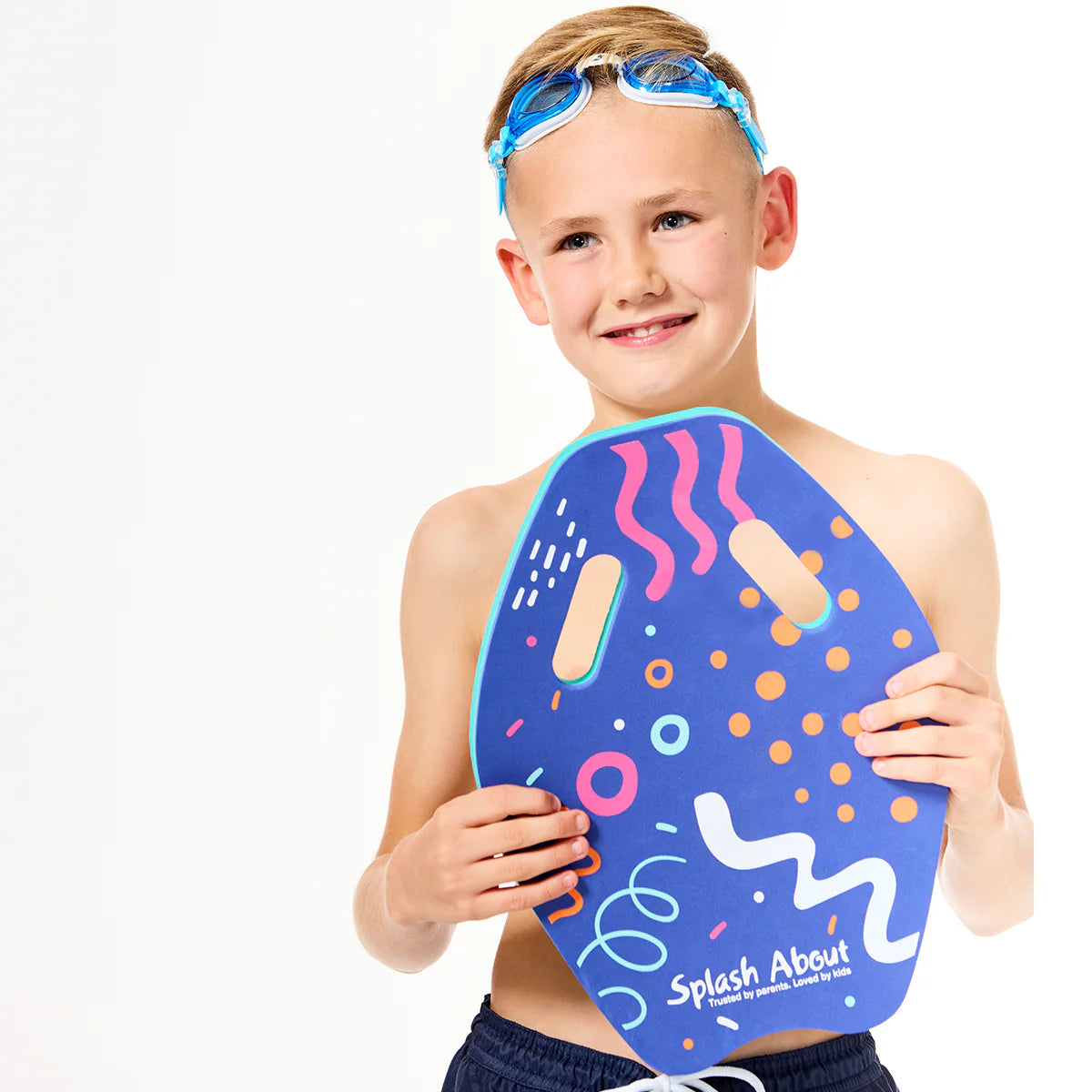 Menino com óculos de natação na testa, sorridente, a segurar a prancha de natação Splash About - Kickboard Junior azul com padrões vibrantes, em fundo branco.