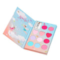 Kit de maquilhagem infantil Souza Elf aberto, mostrando uma paleta de sombras e brilhos labiais em tons rosa, roxo e azul, com aplicadores, dentro de uma caixa em forma de livro ilustrada com fadas.