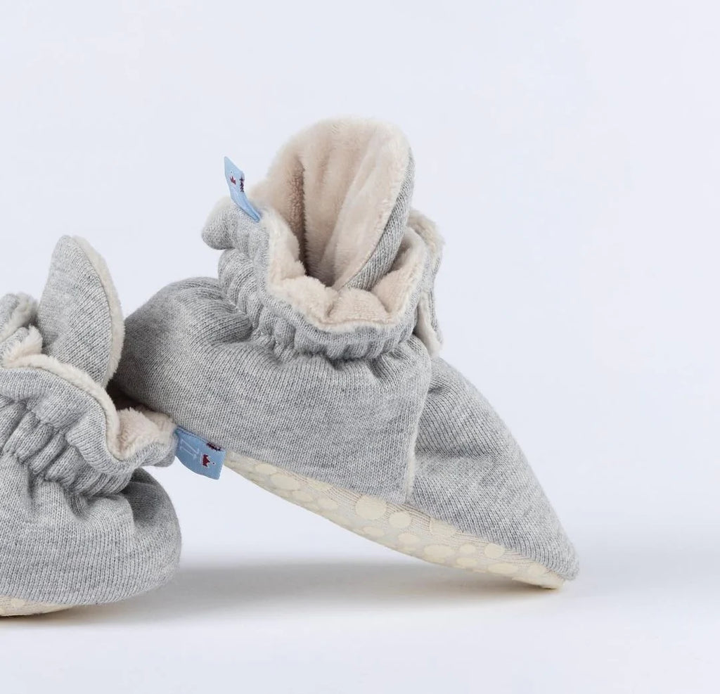 Pantufas cinza com detalhes em azul, feitas para manter os pés do bebé quentinhos e protegidos com um ajuste seguro.

