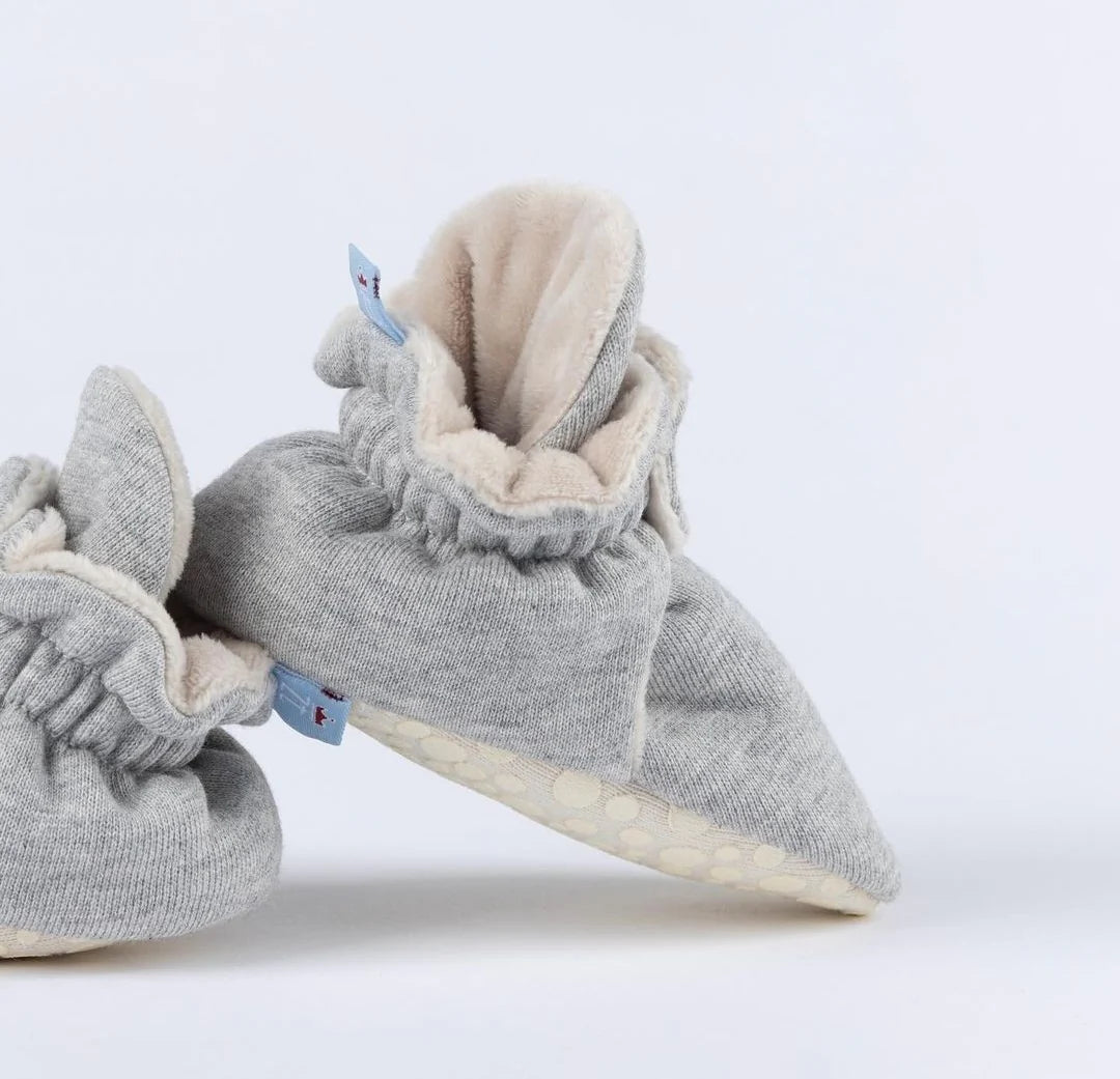 Pantufas cinza com detalhes em azul, feitas para manter os pés do bebé quentinhos e protegidos com um ajuste seguro.
