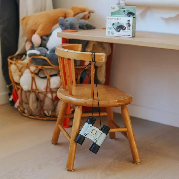 Binóculos Kidywolf Verde pendurados pelo cordão numa cadeira de madeira infantil, num quarto de criança.