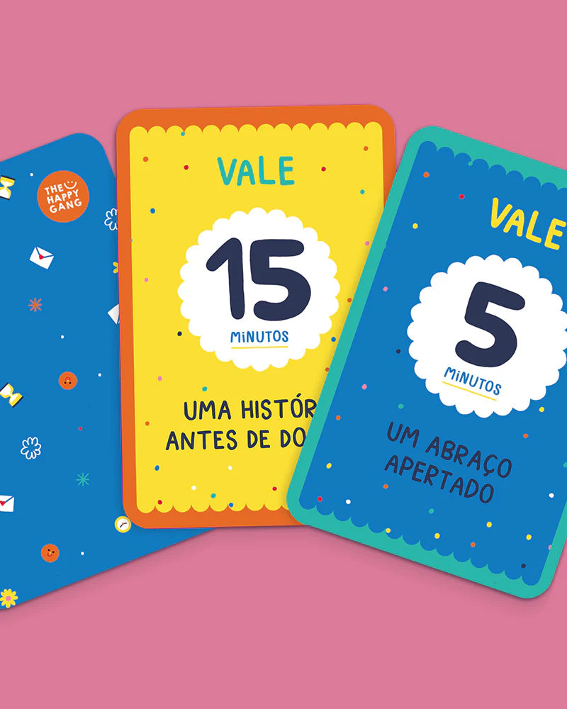 Duas cartas coloridas do jogo 'THE HAPPY GANG - Tens Tempo para Mim?' em destaque, mostrando exemplos de vales: "15 minutos - Uma história antes de dormir" e "5 minutos - Um abraço apertado".
