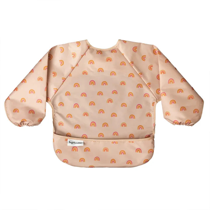 Babete impermeável Tiny Twinkle Rainbow com mangas, em tons pastel de rosa e laranja, com um padrão divertido de pequenos arco-íris, apresentado em fundo branco.